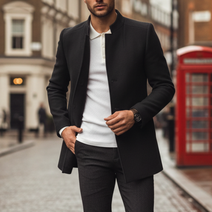 Black coat over a white textured polo and dark pants. The man left hand adjusts the coat.