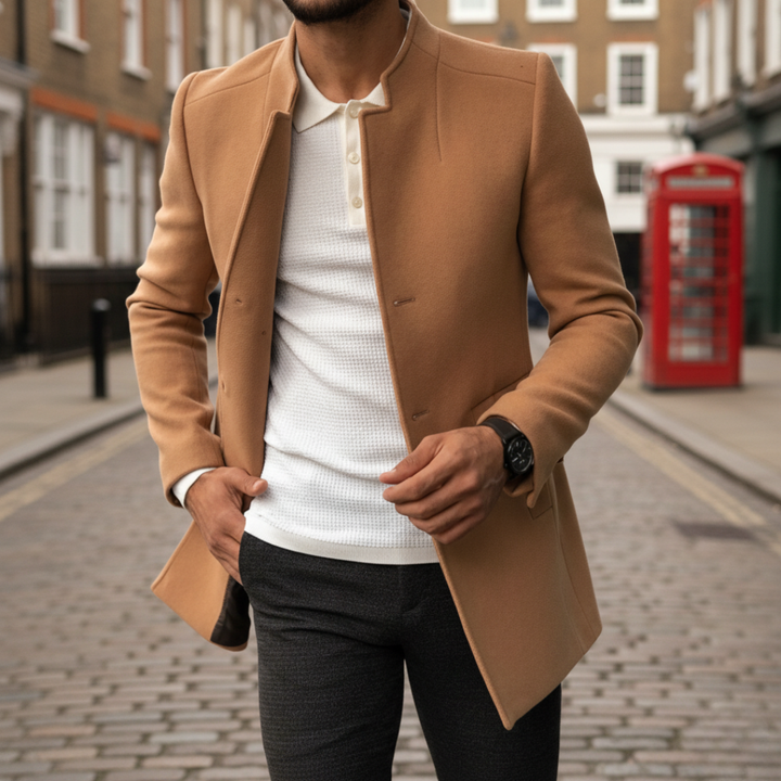 Brown coat over a white textured polo and dark pants. The man left hand adjusts the coat.