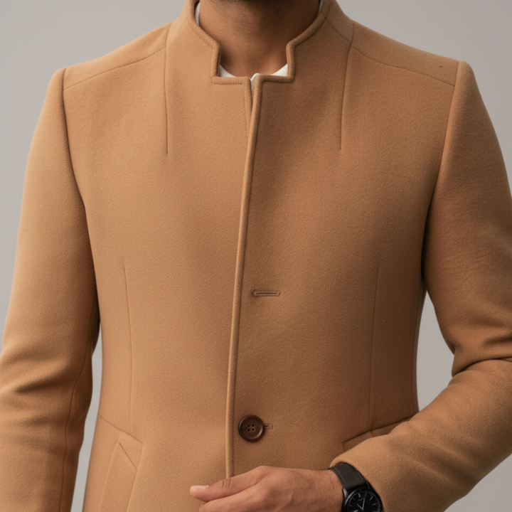 Brown coat close-up details over a white textured polo and dark pants. The man left hand adjusts the coat.