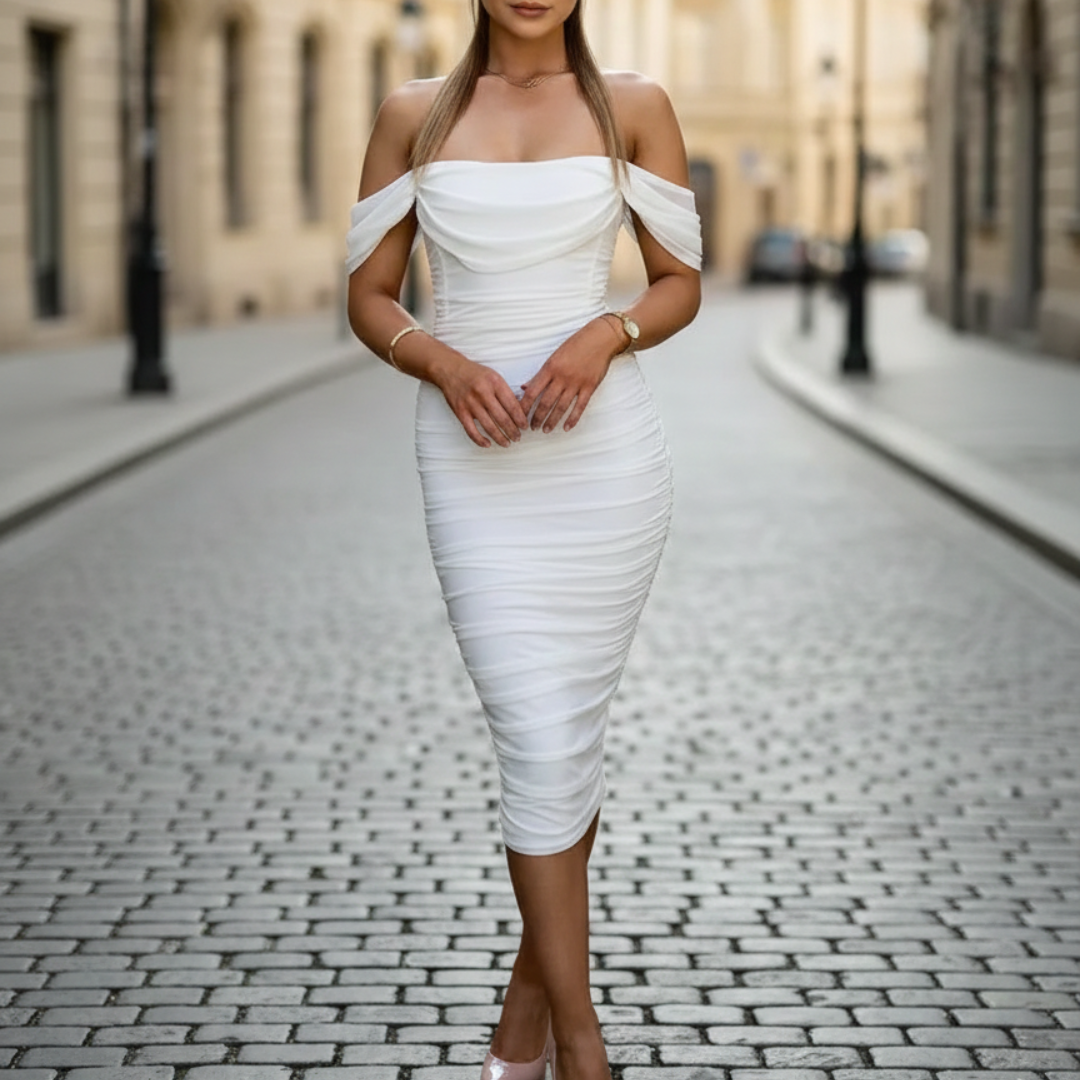 A woman in a white off-shoulder dress stands gracefully on a cobblestone street.

