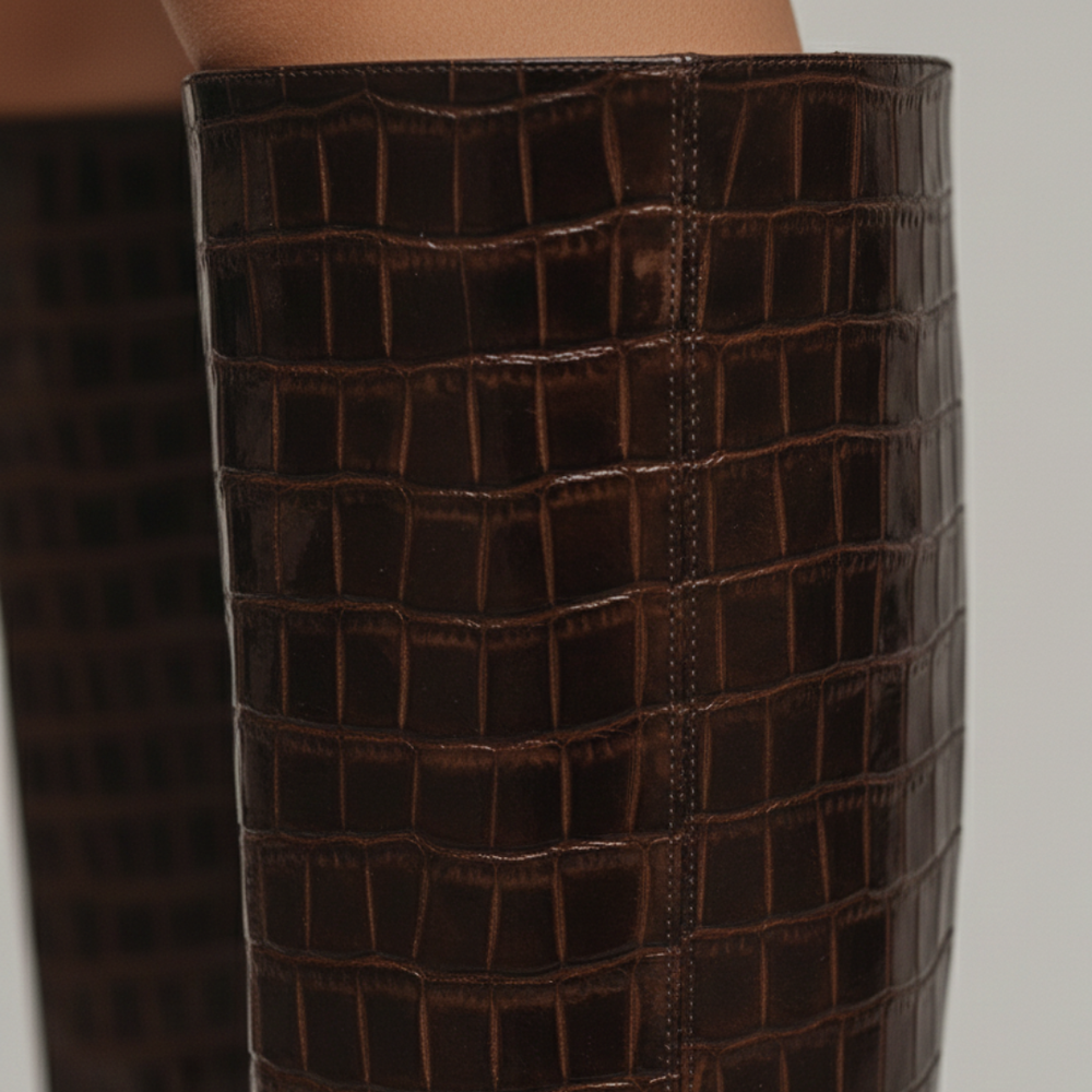 Brown crocodile skin knee-high boots with a slim heel and rounded square toe, good for fall and winter styling.