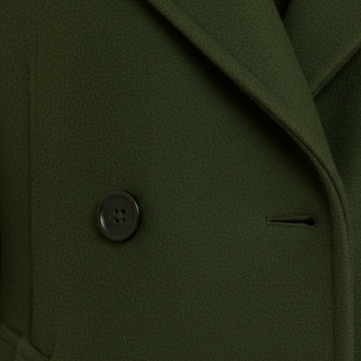 A woman in a knee-length green coat  stands on a cobblestone street, good for cold-weather fashion