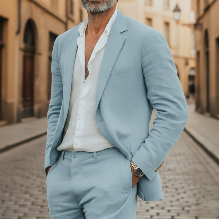 A man in a light blue linen suit stands on a cobblestone street.