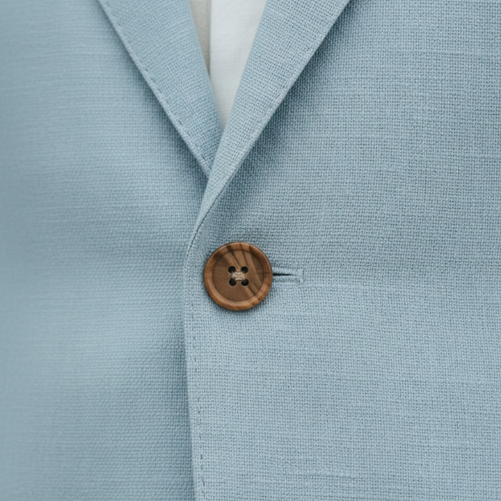 A man in a light blue linen suit stands on a cobblestone street.