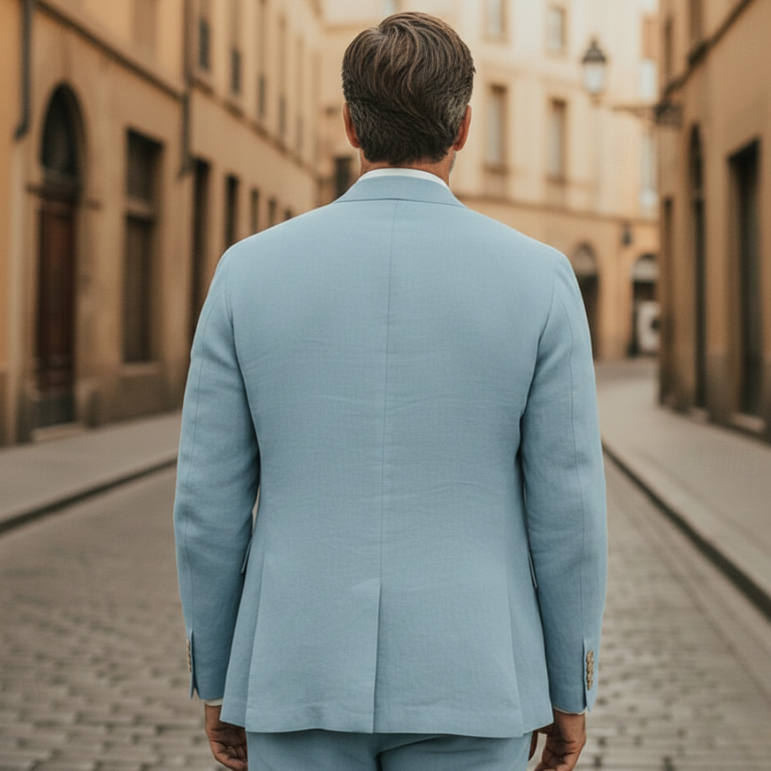 A man in a light blue linen suit stands on a cobblestone street.