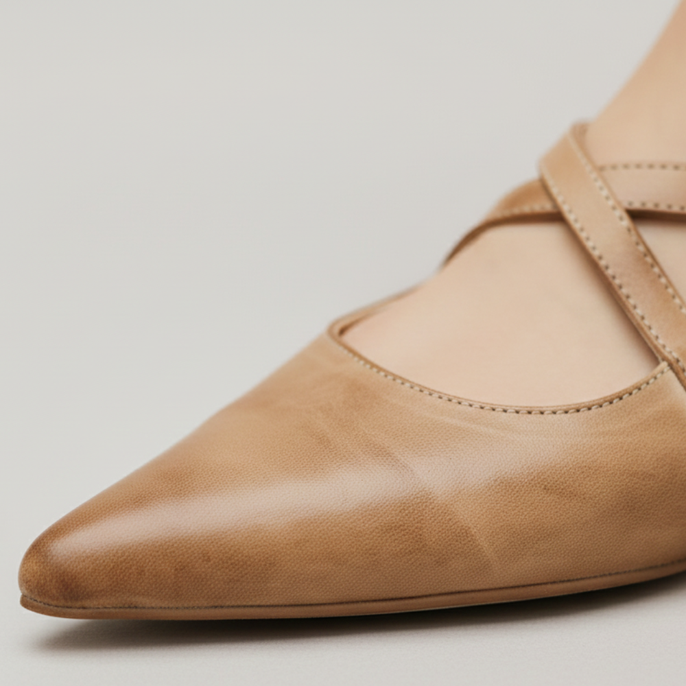 A woman's feet in beige leather pointed mule flats with cross-strap detailing, showcasing a modern and elegant style.