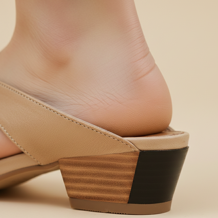 A woman's feet in beige leather pointed mule flats with cross-strap detailing, showcasing a modern and elegant style.