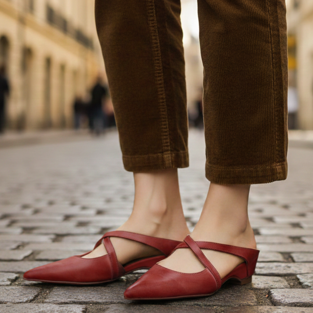 A woman's feet in red leather pointed mule flats with cross-strap detailing, showcasing a modern and elegant style.
