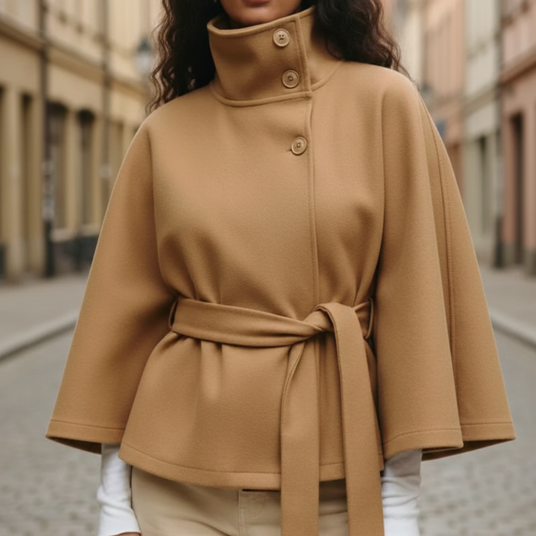 A woman wearing a beige cape jacket over jeans, showcasing a modern and elegant fall outfit with a funnel neckline.
