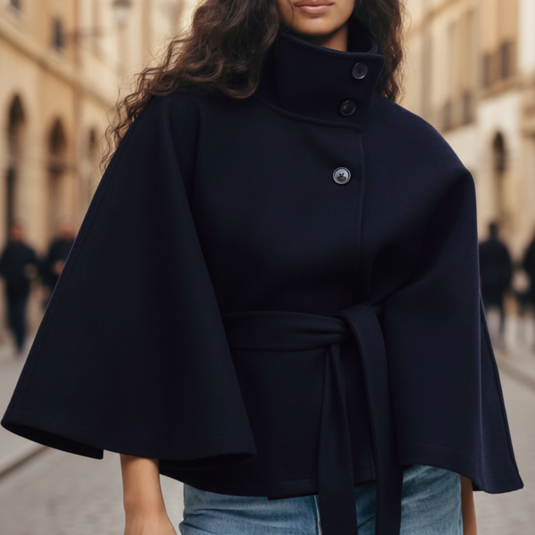 A woman wearing a navy blue cape jacket over jeans, showcasing a modern and elegant fall outfit with a funnel neckline.