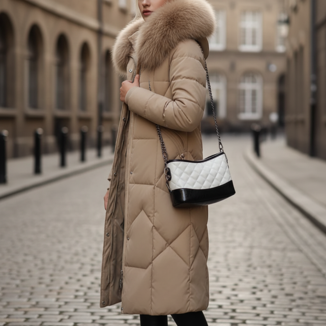  A woman wearing a khaki coat with fur trim stands on a cobblestone street, embodying winter fashion.