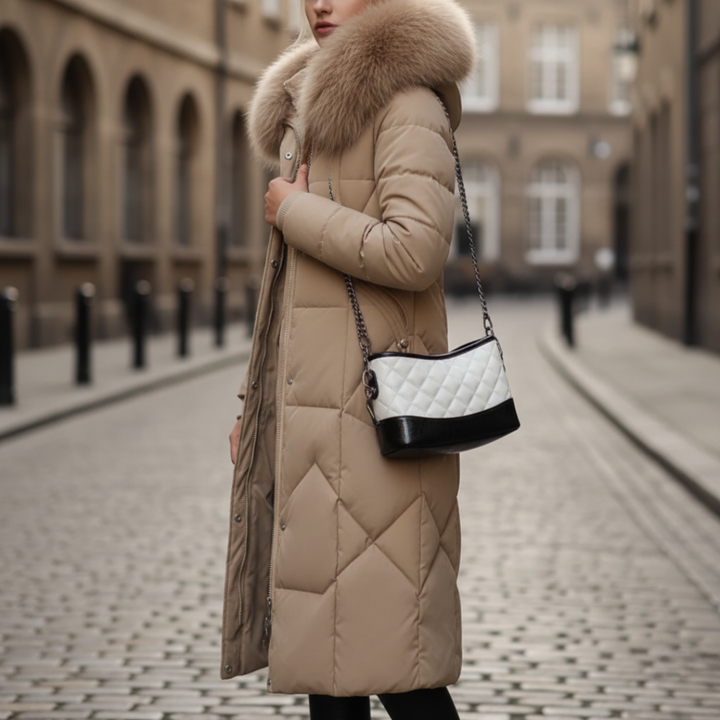  A woman wearing a khaki coat with fur trim stands on a cobblestone street, embodying winter fashion.