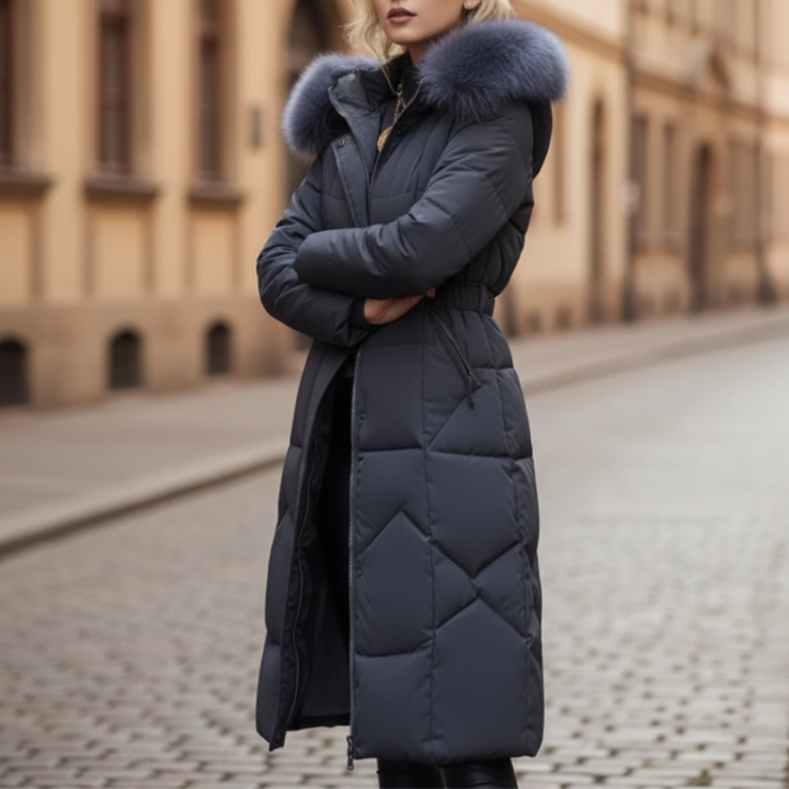  A woman wearing a grey coat with fur trim stands on a cobblestone street, embodying winter fashion.