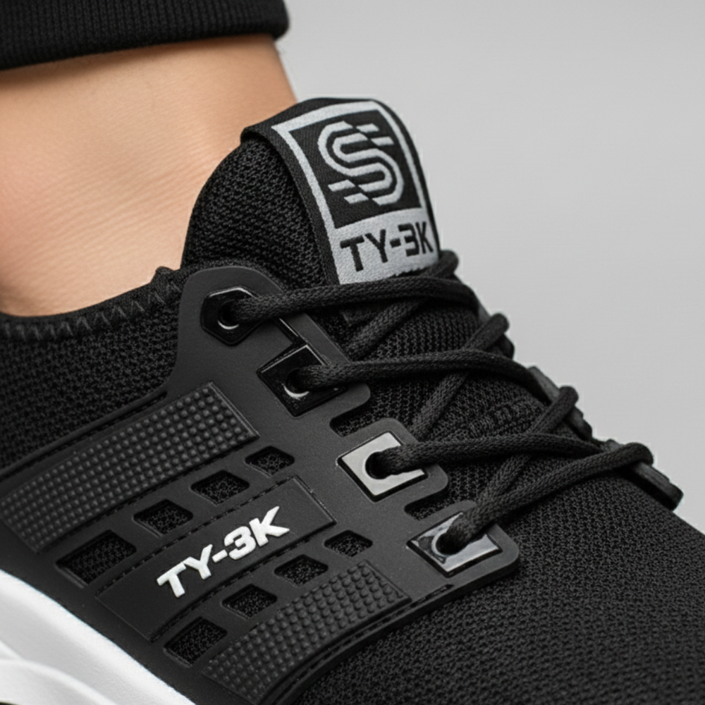  Black and white sneakers resting on a yellow background, featuring a sleek knit upper and cushioned rubber outsole.