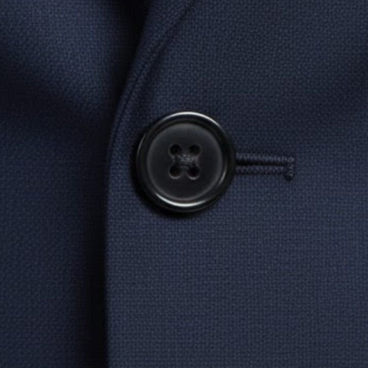 A man in a tailored blue suit stands confidently on a cobblestone street, showing elegance and modern style.

